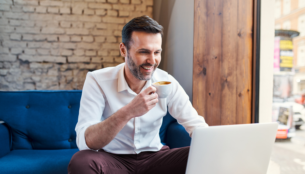 man in white buttoned shirt smiling in front of laptop